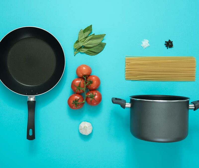 kitchen pots and pans, pasta, tomatos, basil on a blue background